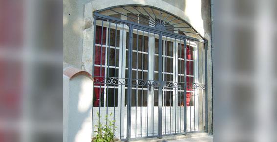 Fenêtre avec barreaux de sécurité en fer forgé ; rideaux rouges visibles à travers la vitre.