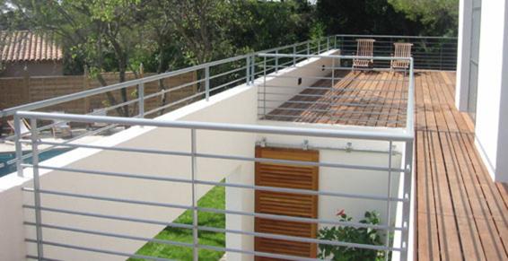 Balcon avec rambarde métallique donnant sur une terrasse en bois et un carré de pelouse.