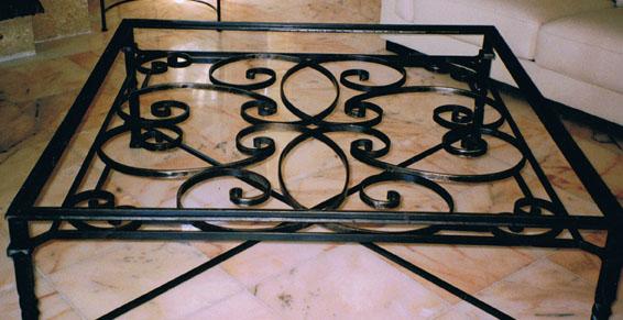 Table basse en fer forgé noir ornée de volutes décoratives, posée sur un sol carrelé.