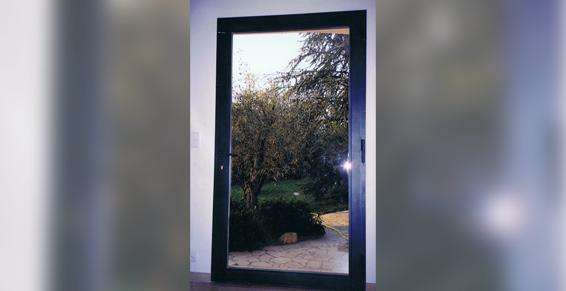 Porte à cadre noir laissant apparaître une vue floue d'une cour arrière avec des arbres et un chemin.