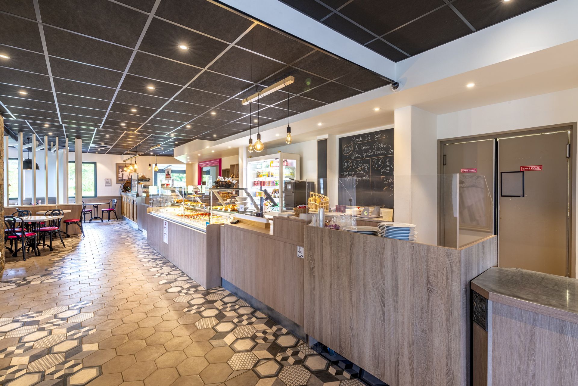 L'intérieur d'un café moderne comprend un long comptoir, un carrelage à motifs et un plafond sombre avec éclairage encastré.