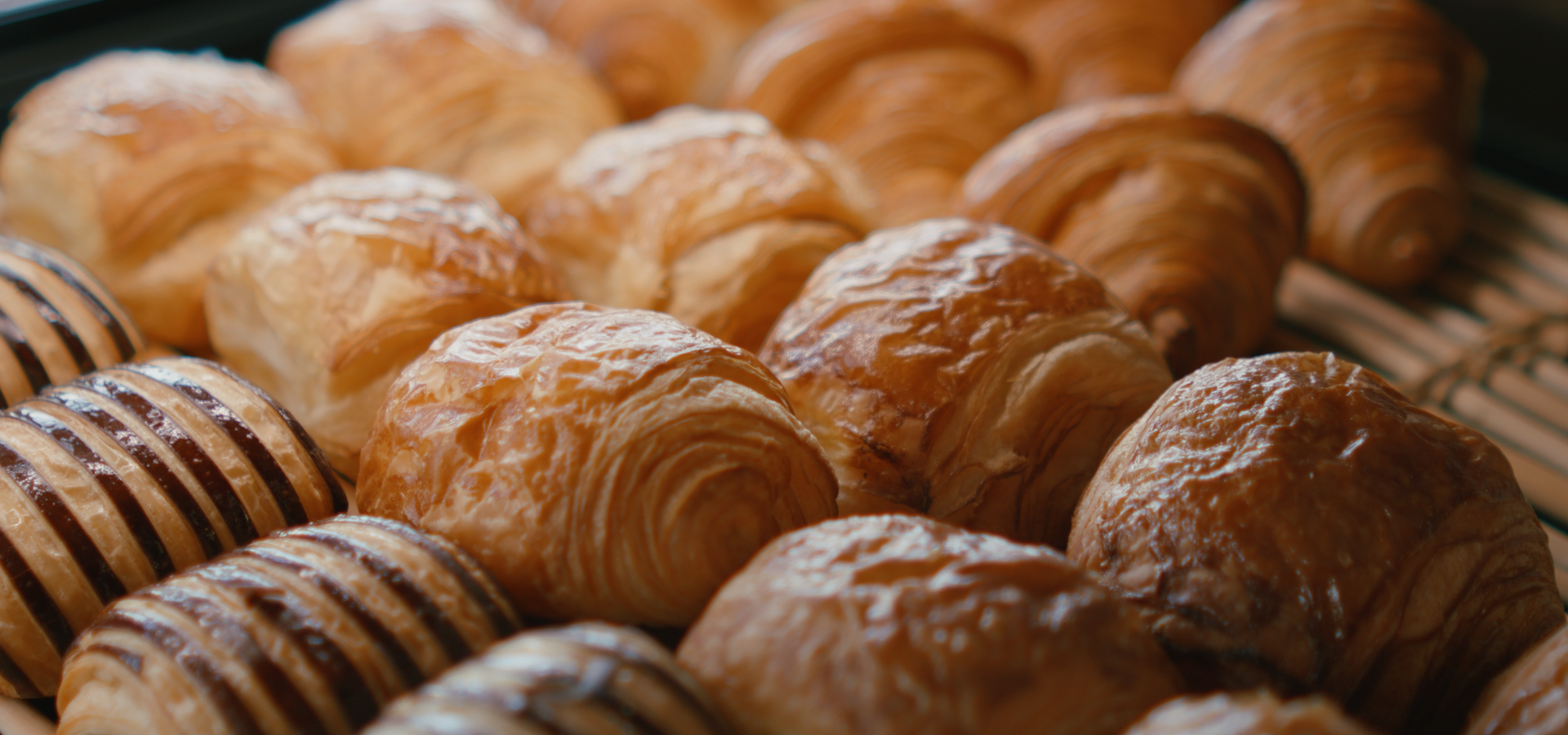 Un étalage de viennoiseries fraîchement cuites et dorées, comprenant des petits pains nature et des friandises rayées au chocolat, présenté sur un support métallique.