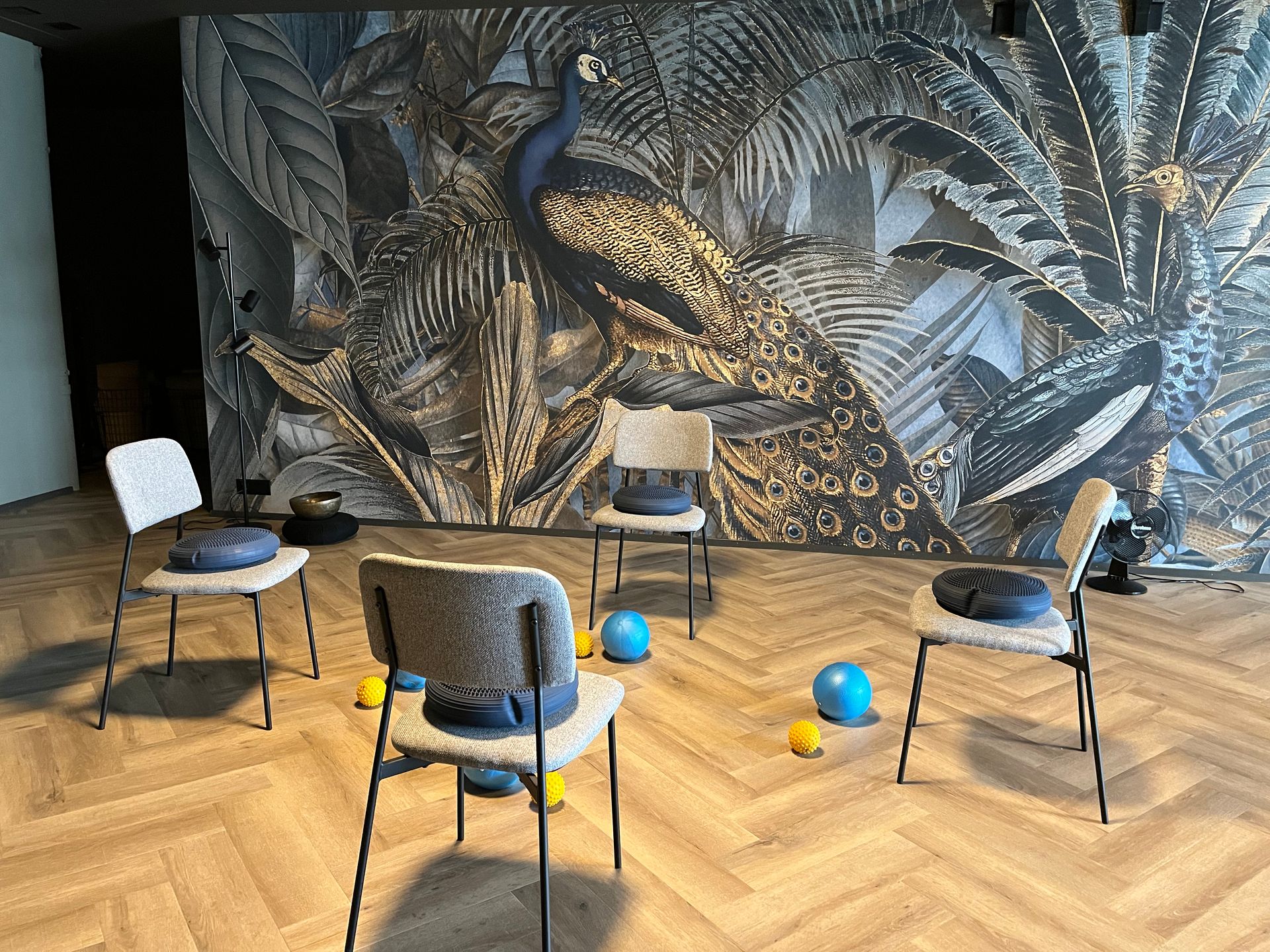 Vier Stühle mit Kissen im Kreis angeordnet. Im Hintergrund ist ein Wandgemälde mit einem Pfau zu sehen.
