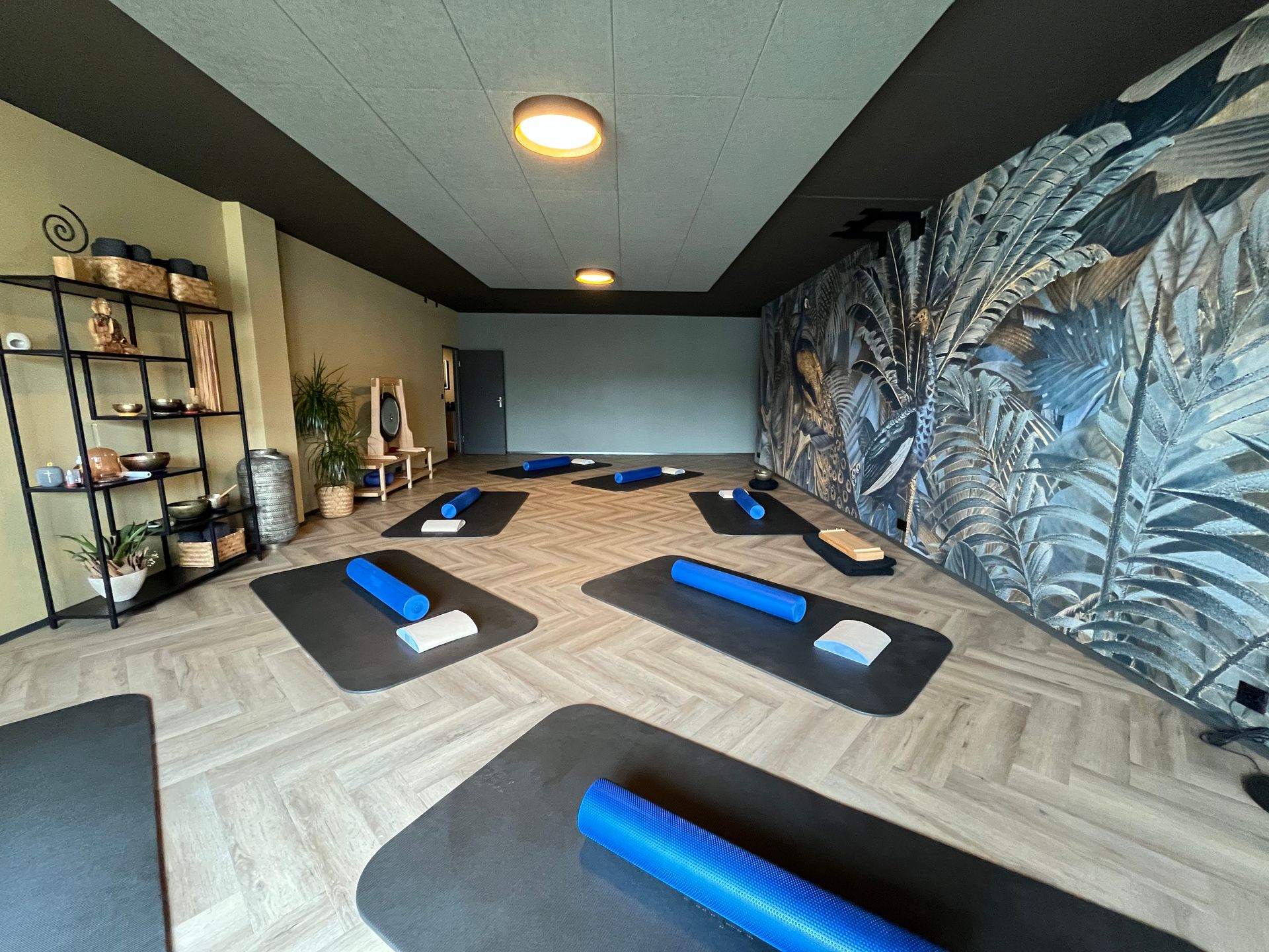 Yogastudio mit Matten, Schaumstoffrollen und Blumentapete; neutrale Farben.