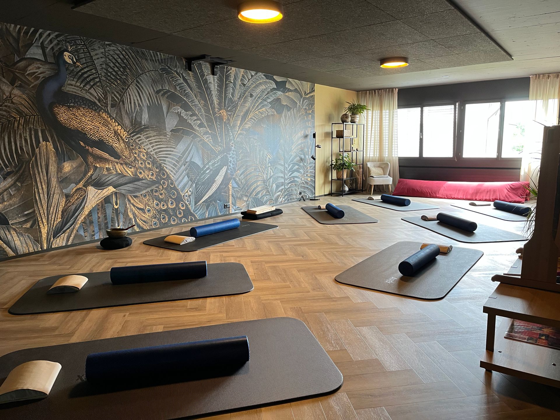 Yogastudio mit Matten, Schaumstoffrollen und einer Wand mit Pfauenmotiv.
