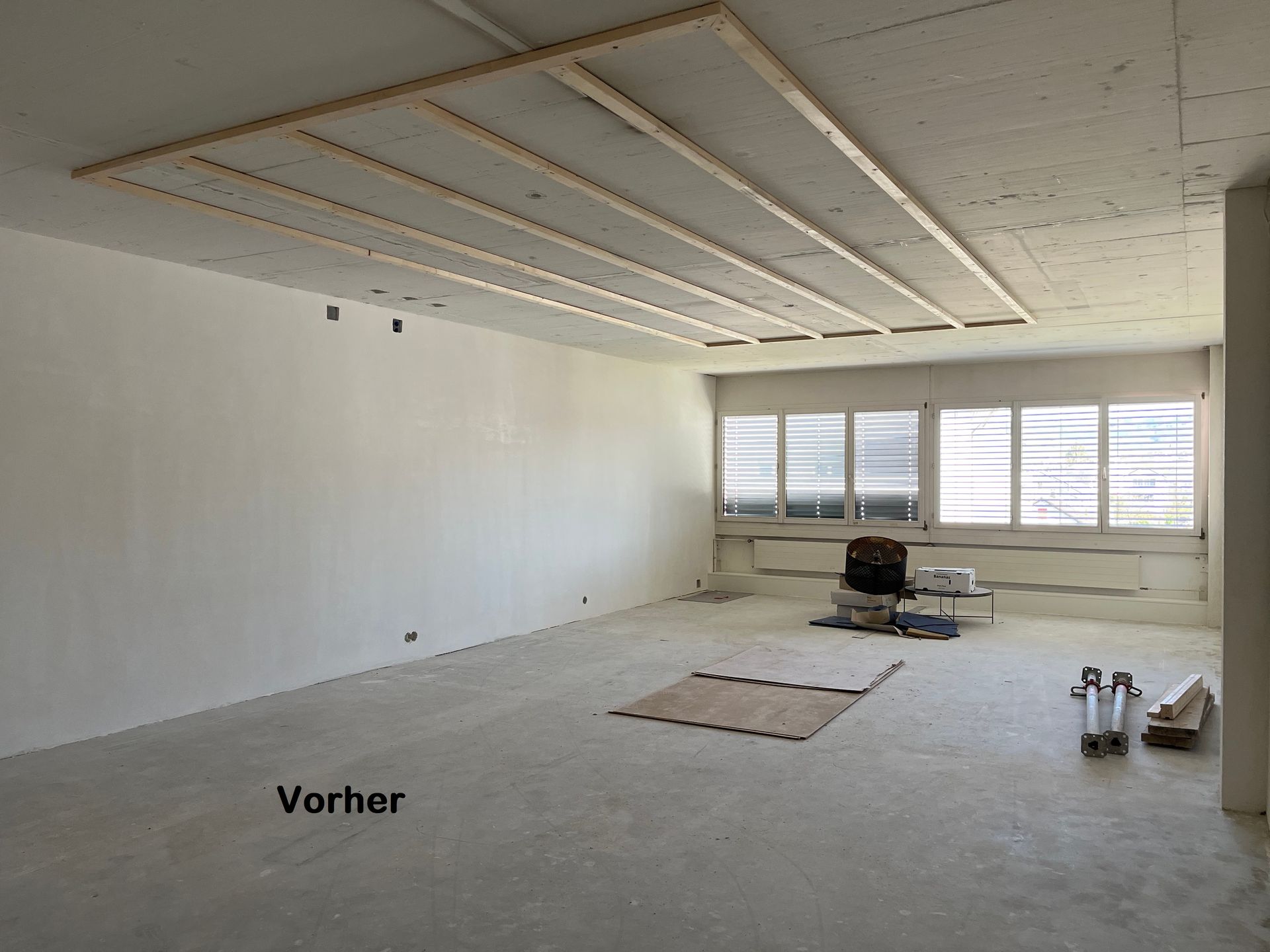 Leerer Raum im Bau, mit freiliegenden Deckenbalken und unfertigen Wänden, hellgraue Farbe.