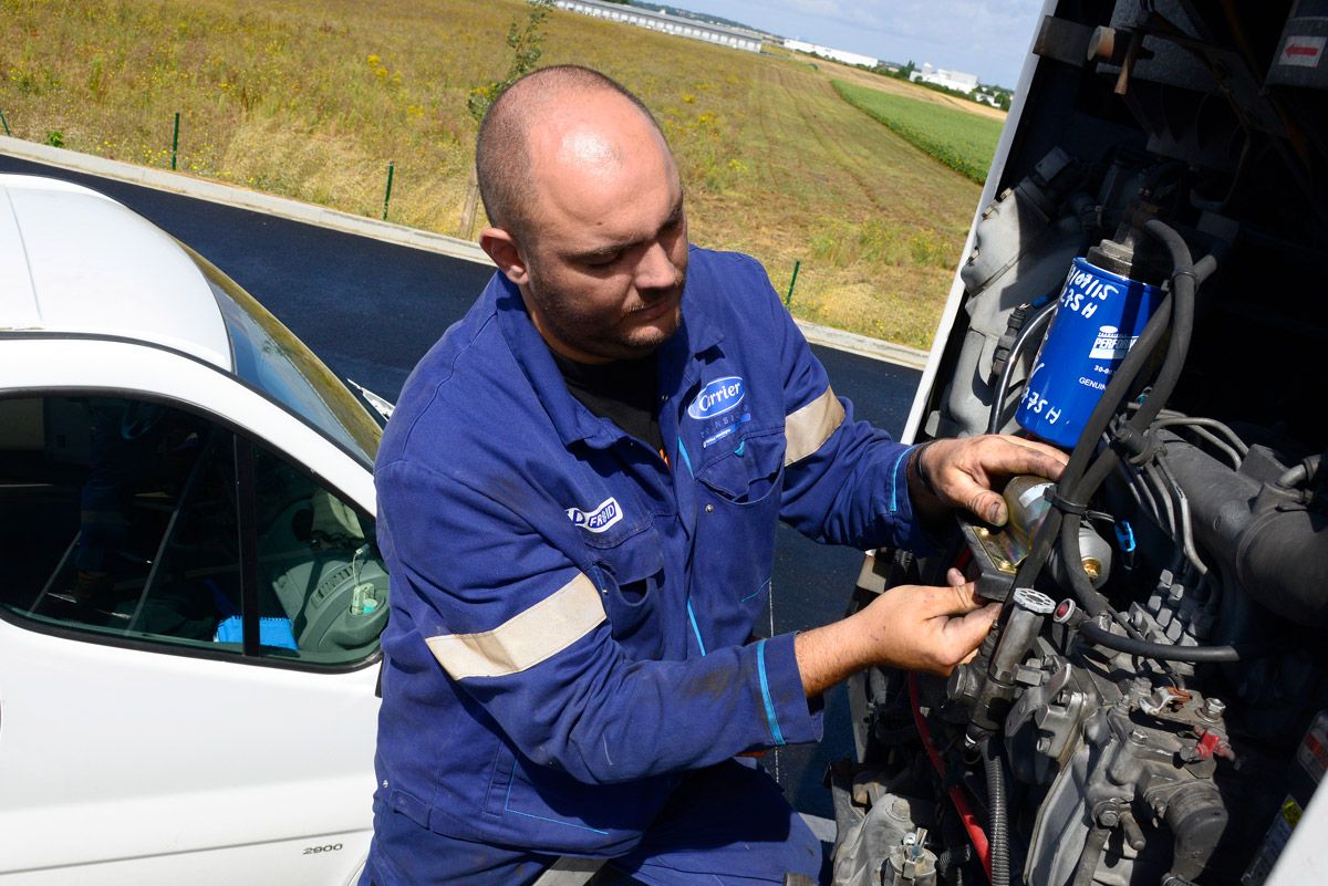 Un mécanicien en combinaison bleue travaille sur un moteur d'avion à côté d'un avion blanc sur une piste