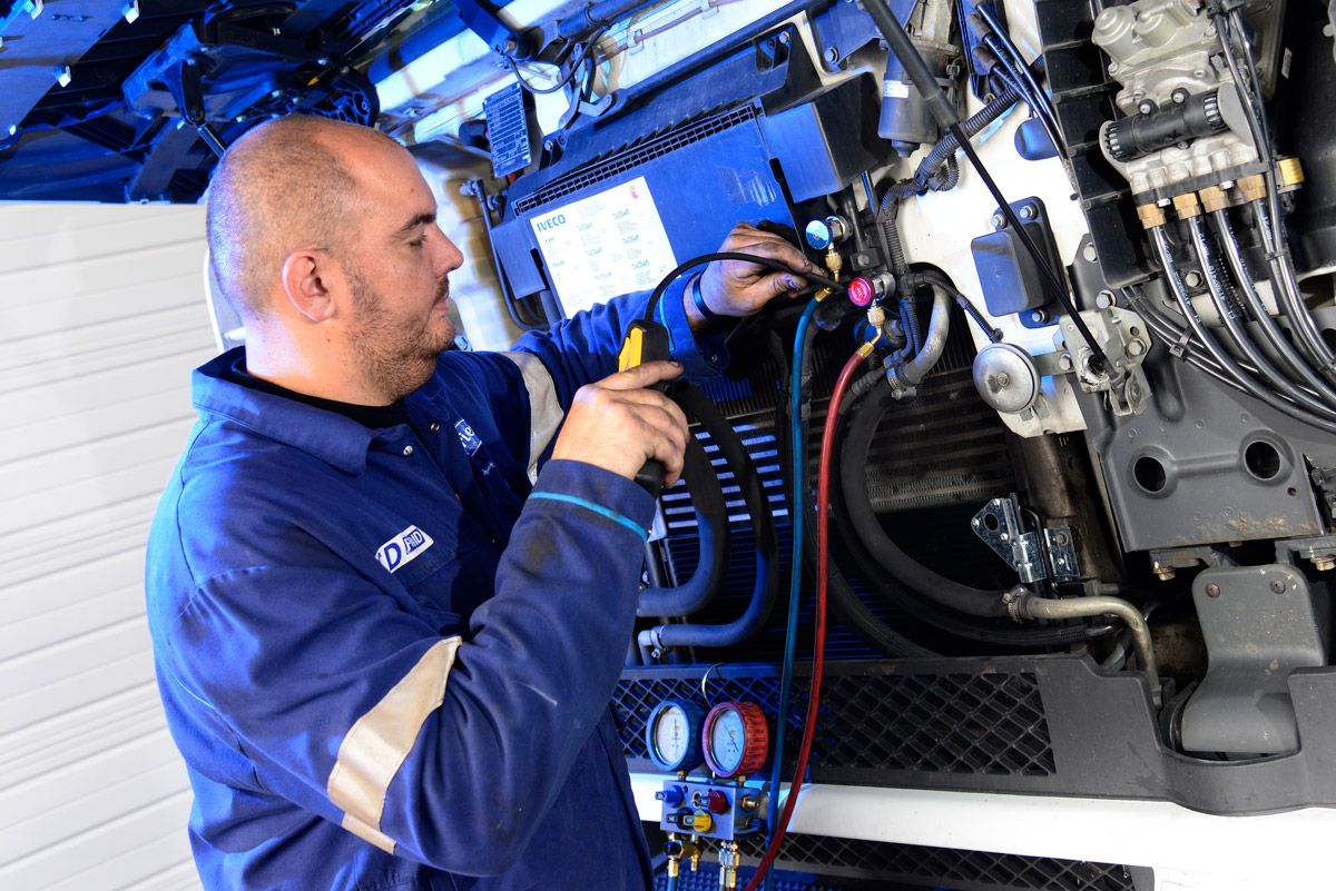Un mécanicien en combinaison bleue inspecte le câblage du moteur dans un garage