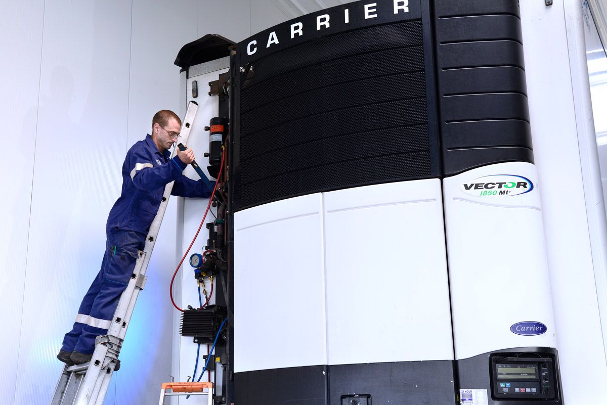 Un technicien effectue la maintenance d'une grande unité de climatisation Carrier depuis une échelle dans une buanderie