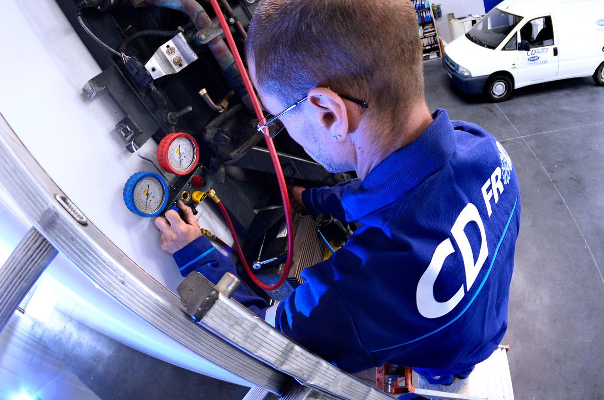 Un technicien en chemise de travail bleue vérifie les manomètres et les tuyaux d'un équipement industriel dans un atelier