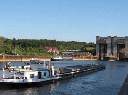 Ein Lastkahn fährt einen Fluss hinunter, im Hintergrund ist eine Brücke