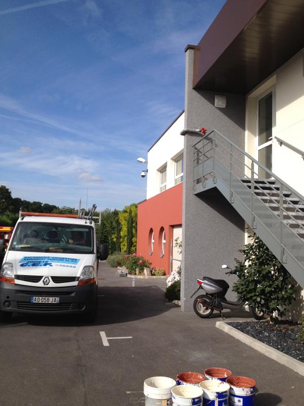 Immeuble avec murs rouges, blancs et gris. Escalier métallique et ciel bleu. 