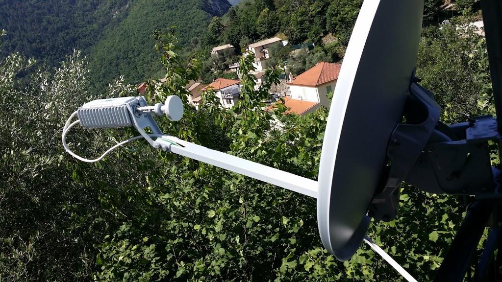 Une antenne parabolique et un récepteur montés à l'extérieur, avec une ville et des arbres en arrière-plan.