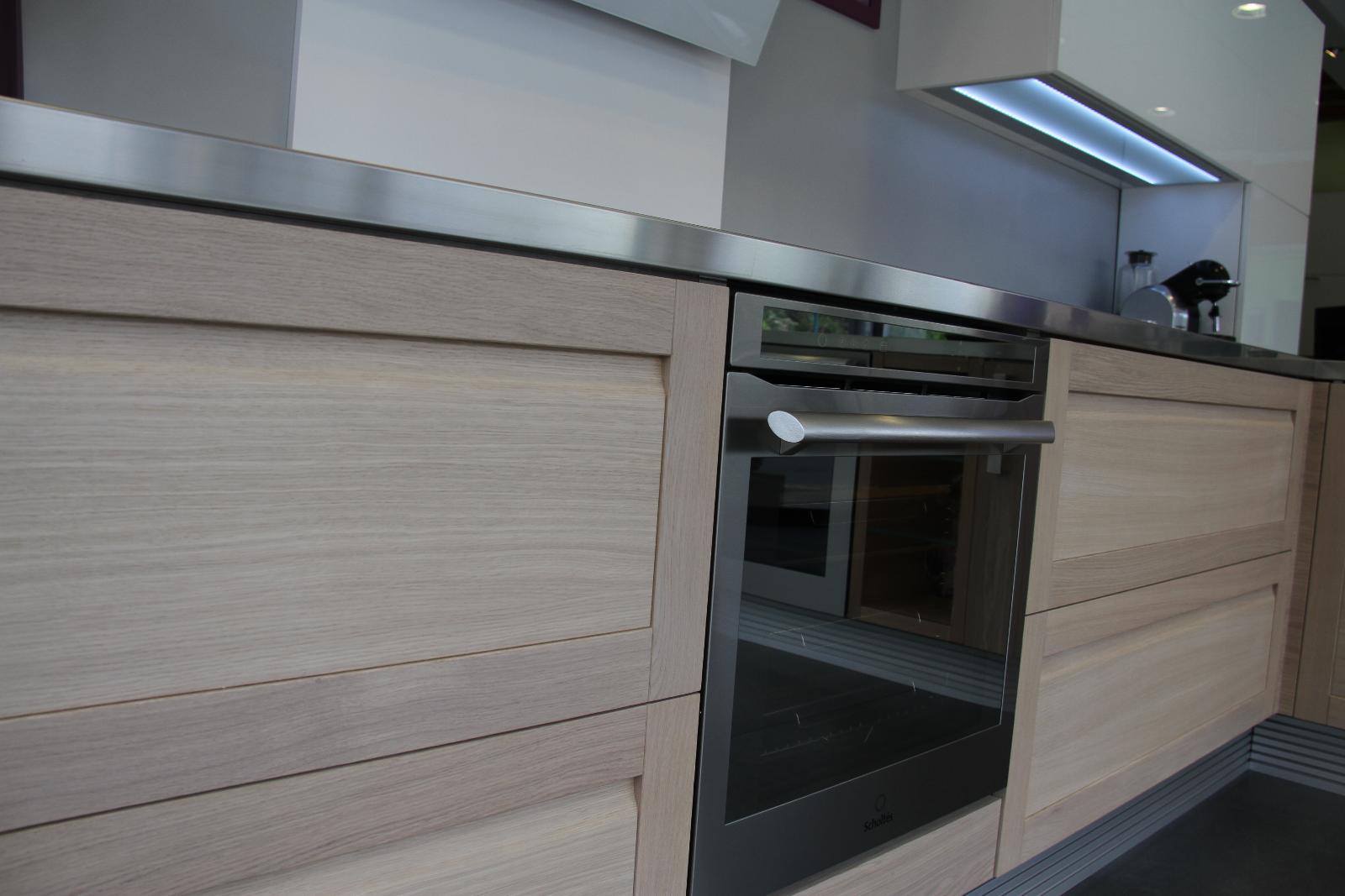 Cuisine moderne avec armoires en bois clair, comptoir en acier inoxydable et four encastré.