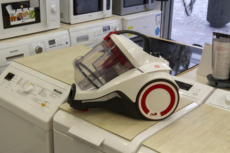 Aspirateur blanc et rouge exposé, entouré d'appareils électroménagers dans un magasin.