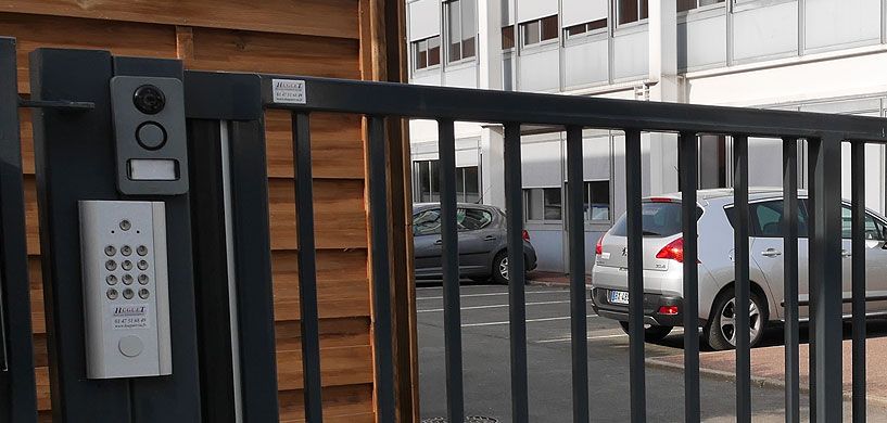 Portail d'immeuble avec digicode et interphone à côté des voitures garées sur le parking