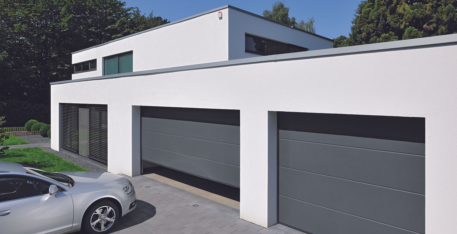 Maison blanche moderne avec trois portes de garage grises et une voiture argentée devant
