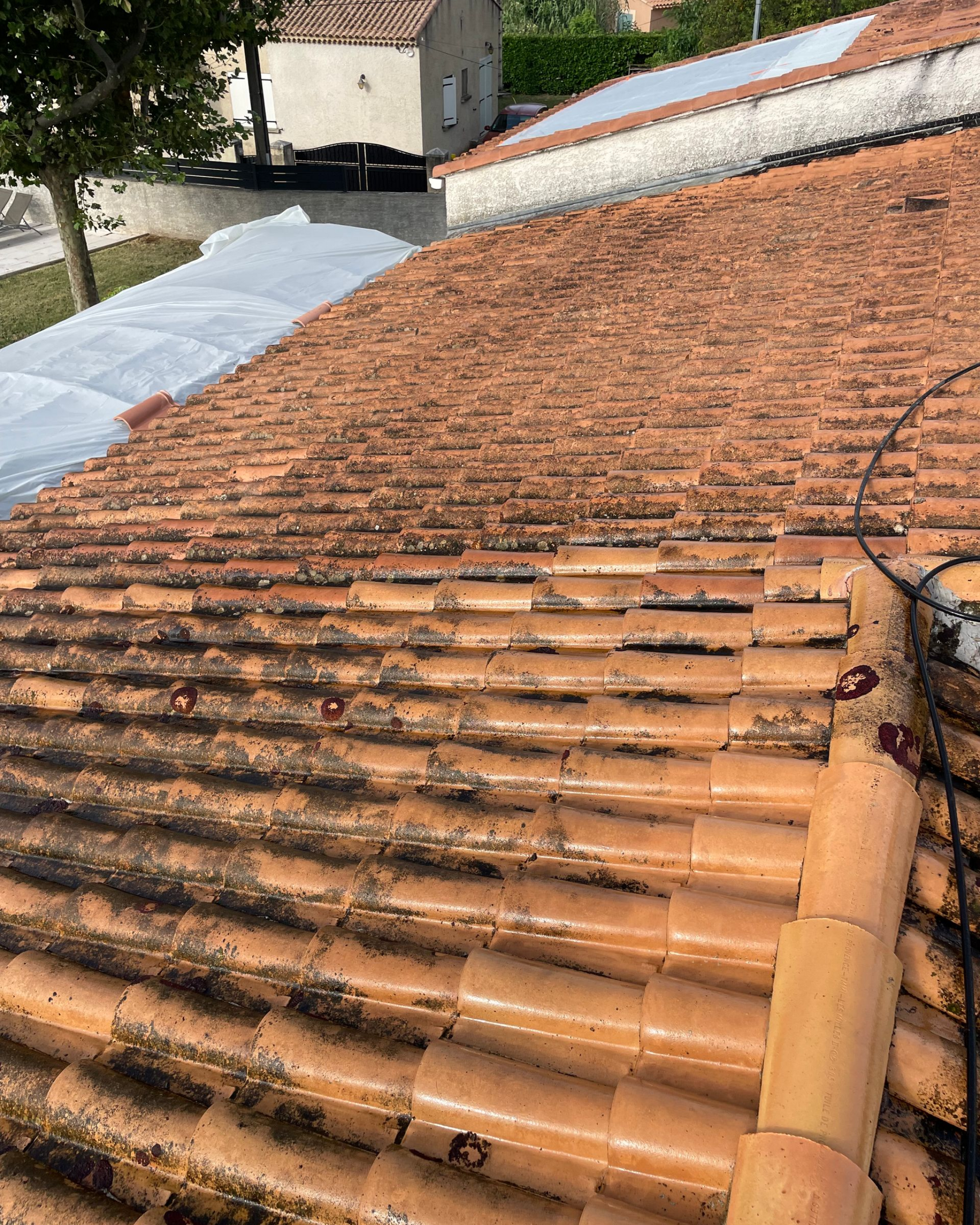 Toit de tuiles rouge orangé patiné par le temps et parsemé de taches de mousse sombre, vu d'en haut près du bord du toit.