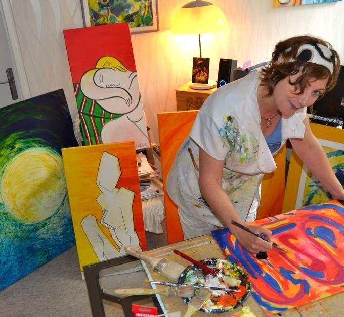 Un artiste peint une toile colorée lors d'un atelier, penché sur une table avec des pinceaux et de la peinture.