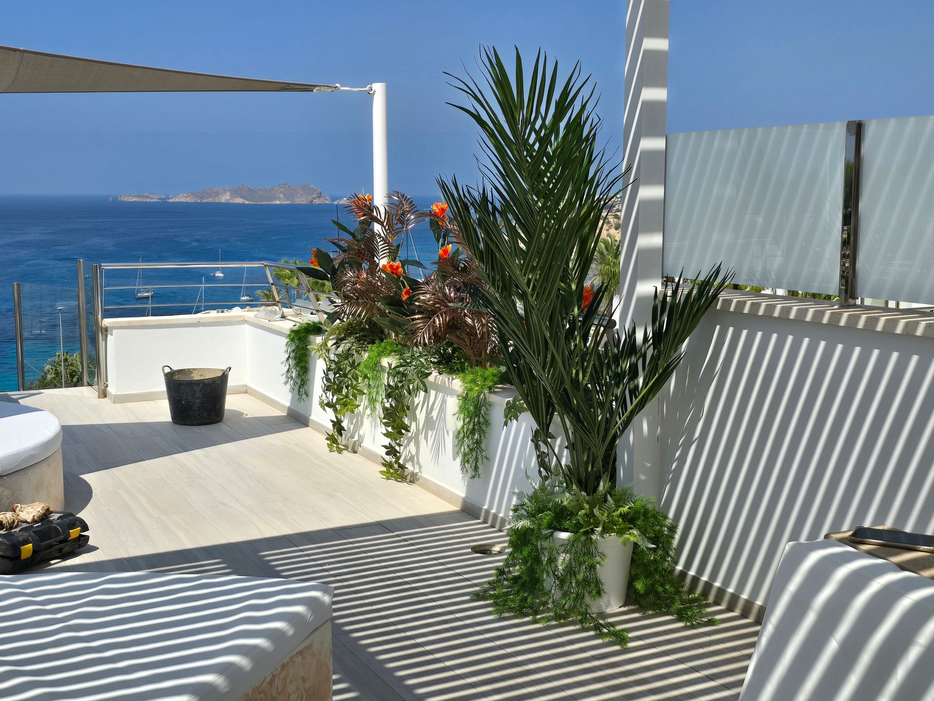 Terraza con vista al mar con plantas, sombrilla y sombras ligeras.