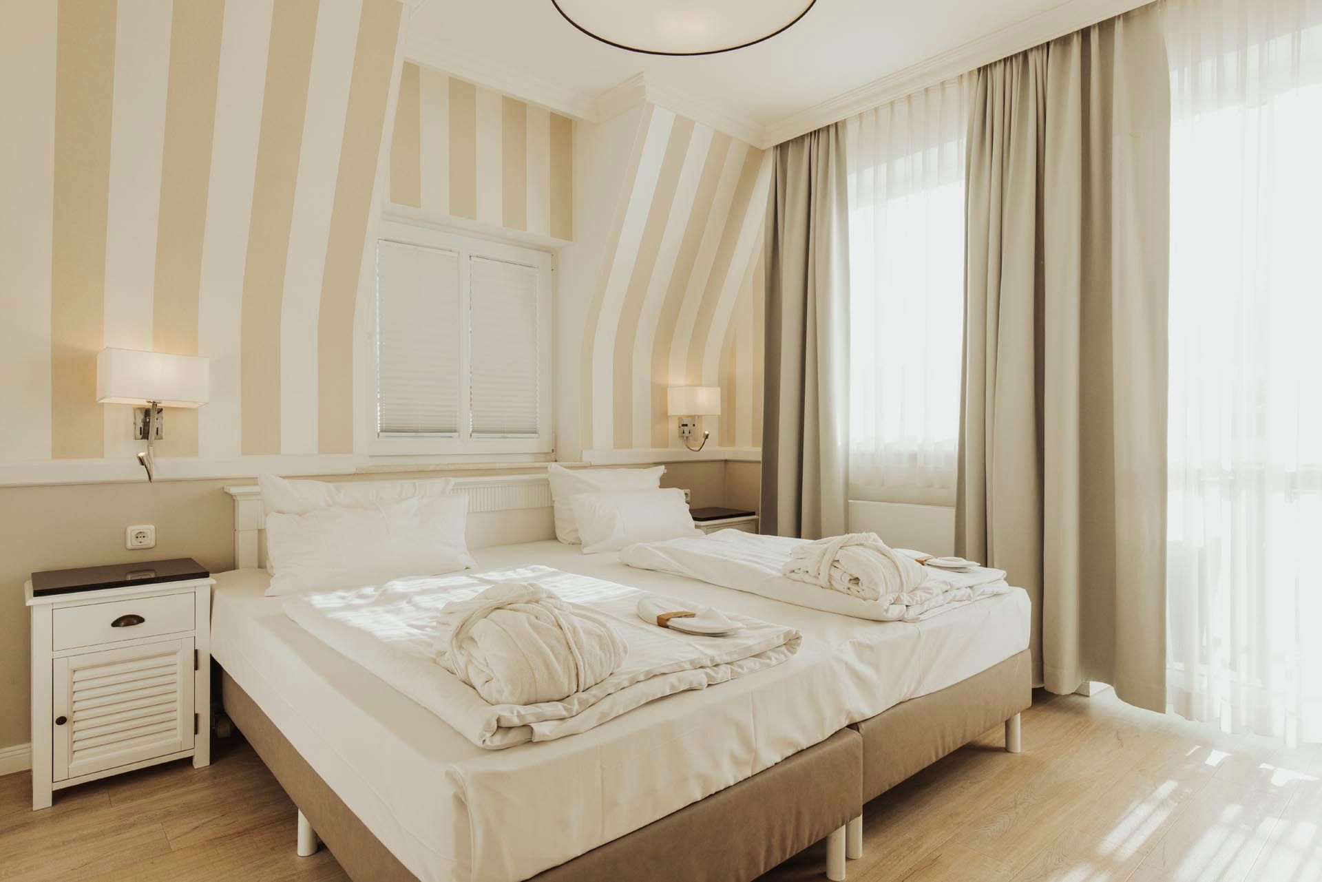 Helles, beigefarbenes Schlafzimmer mit großem Bett, gestreifter Tapete und transparenten Vorhängen.