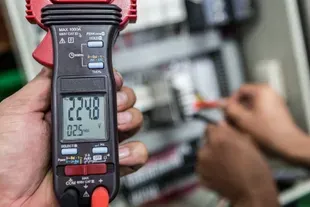 Eletricista usando um multímetro para medir a voltagem em um painel de controle, mostrando 224,8 V.