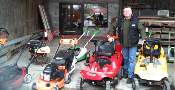 Le gérant du magasin aux côtés des tondeuses en vente au dehors du magasin.