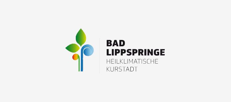 Logo für Bad Lippspringe. Zeigt eine stilisierte Pflanze mit grünen Blättern und einem blauen Wirbel. Text rechts daneben.