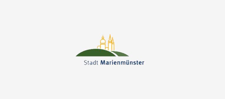 Logo der Stadt Marienmünster mit einem grünen Hügel, auf dem Gebäude stehen, und dem Stadtnamen darunter.