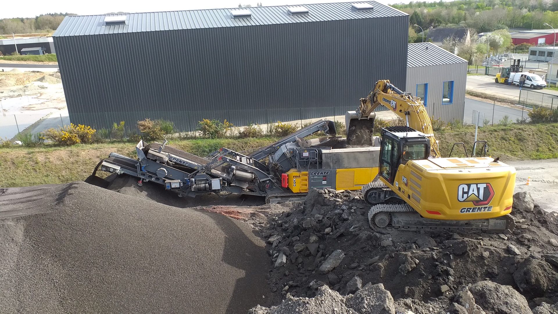 Une pelle mécanique CAT charge des matériaux dans une installation de criblage mobile sur un chantier de construction.