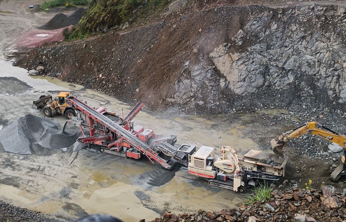 Engins lourds dans une carrière : concasseur de pierres, excavatrice et tas de gravier.