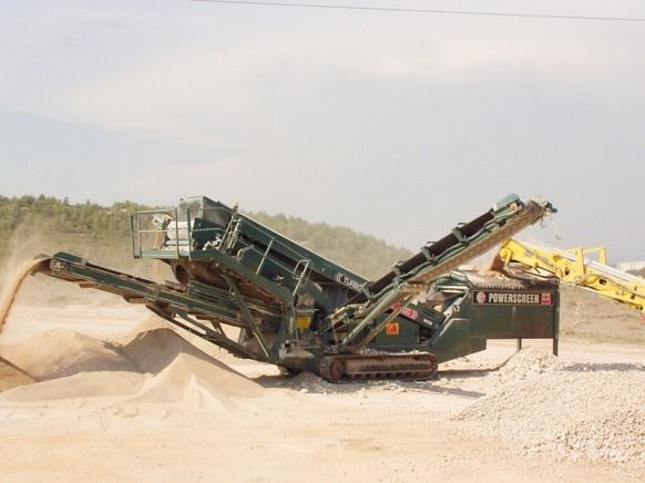 Un concasseur de pierres mobile sur un chantier, équipé de convoyeurs à bande, produit des tas de pierres concassées.