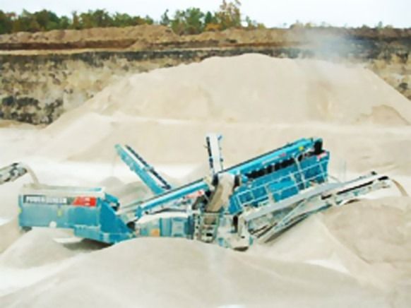 Machine industrielle bleue dans une carrière, traitant du sable ; des monticules de sable entourent la machine.