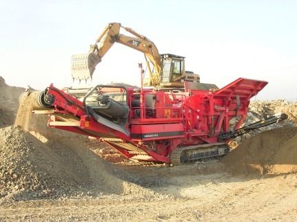Concasseur de roche rouge avec excavatrice dans une carrière, traitant du gravier.