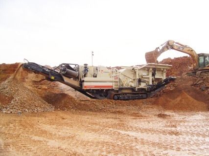 Concasseur de roche mobile traitant des matériaux sur un chantier de construction ; excavatrice déposant des matériaux.