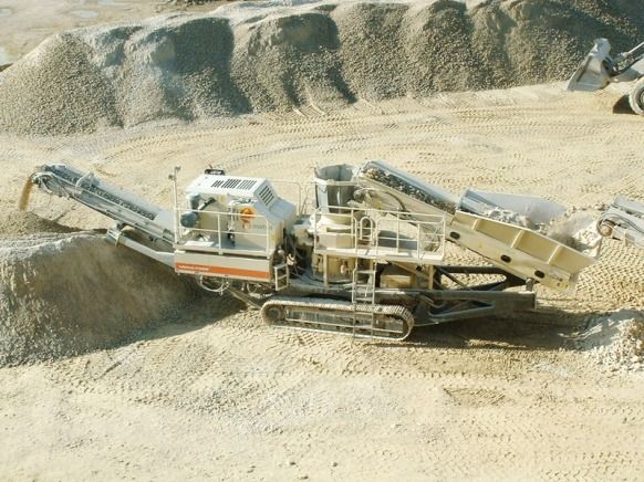 Concasseur de roches mobile sur un chantier de construction, traitant des pierres et du gravier.