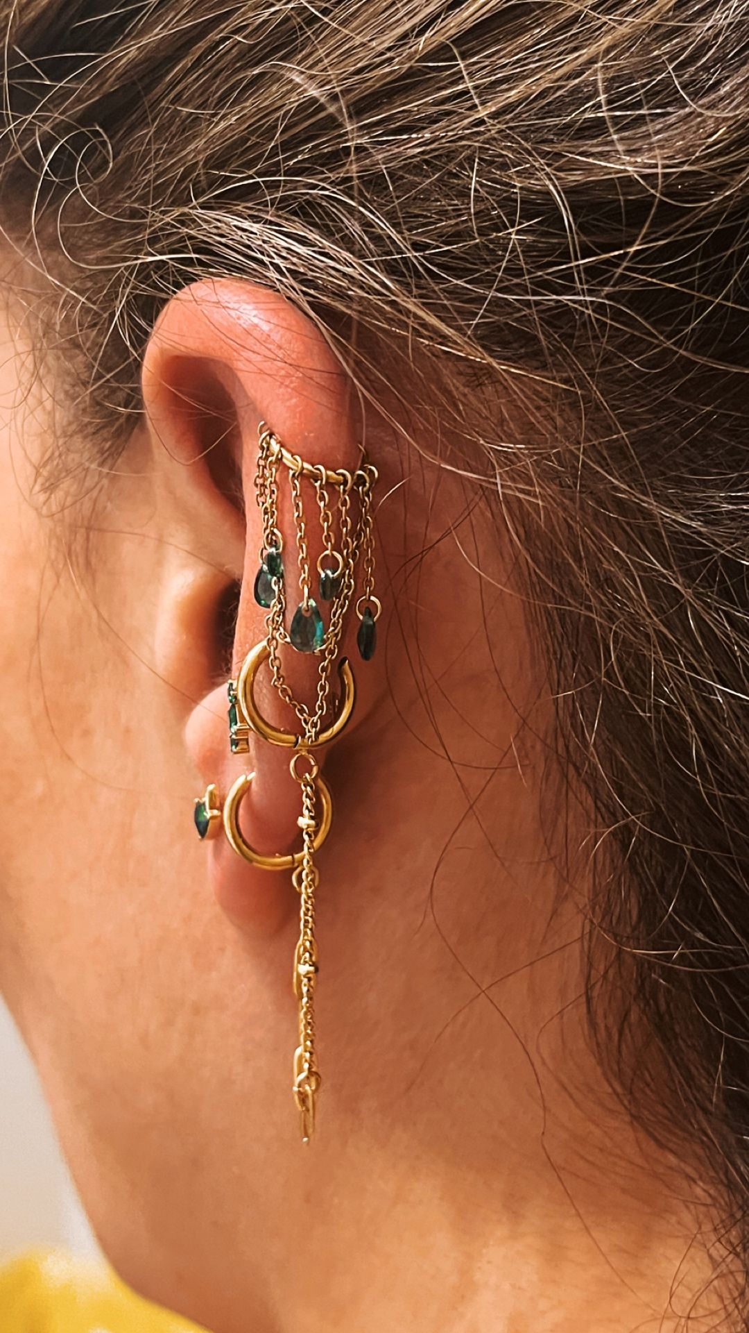 Une oreille percée avec des bijoux or intégrant une pierre verte