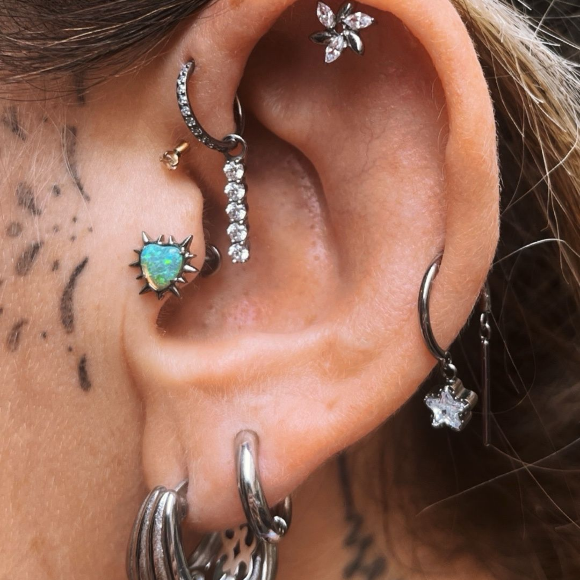 Une femme avec un tatouage à côté de l'oreille ayant de nombreux piercings à l'oreille