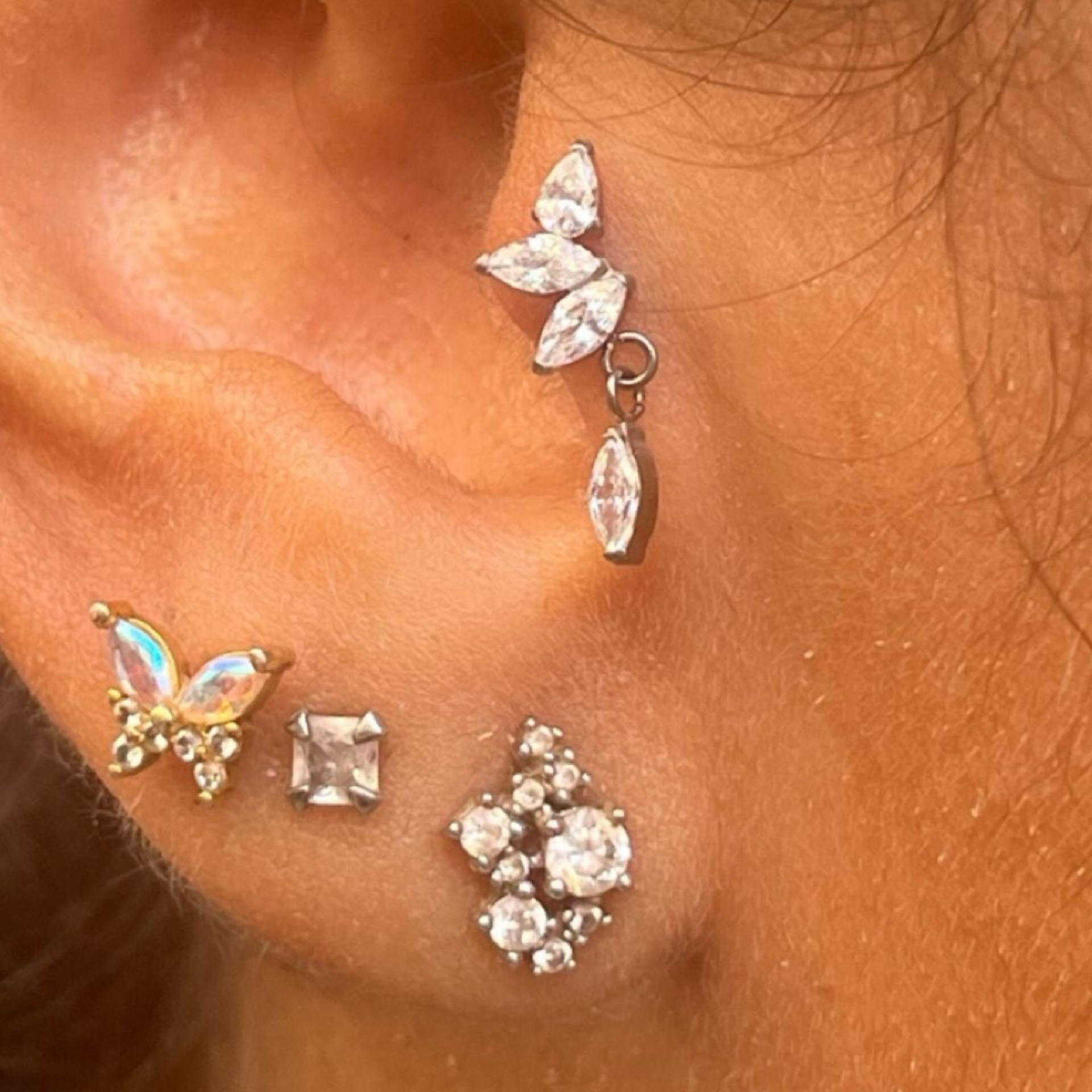 Plusieurs piercings à l'oreille, trois bijoux simples et un en forme de papillon