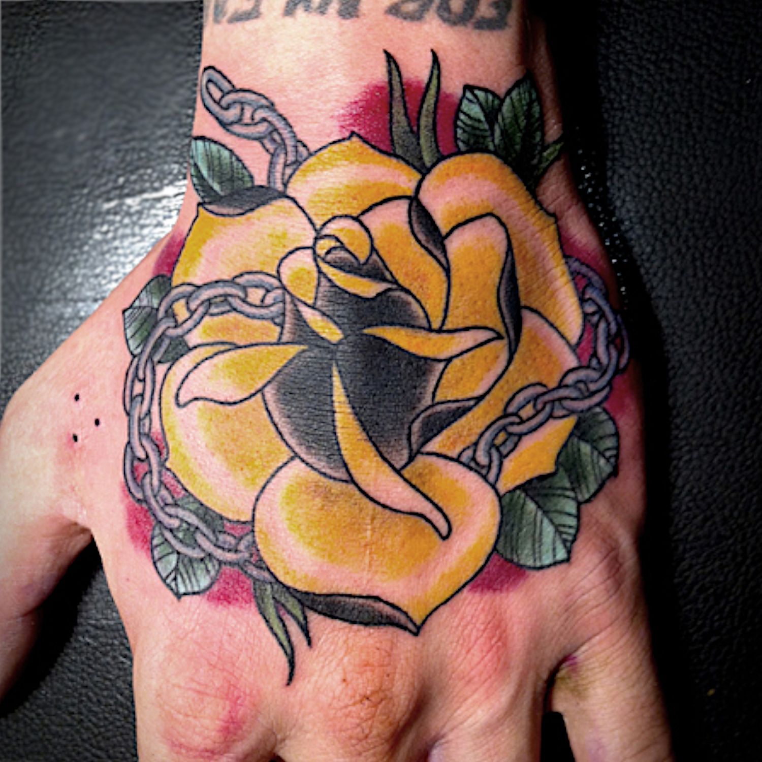 Une rose jaune tatouée avec des chaînes sur la main