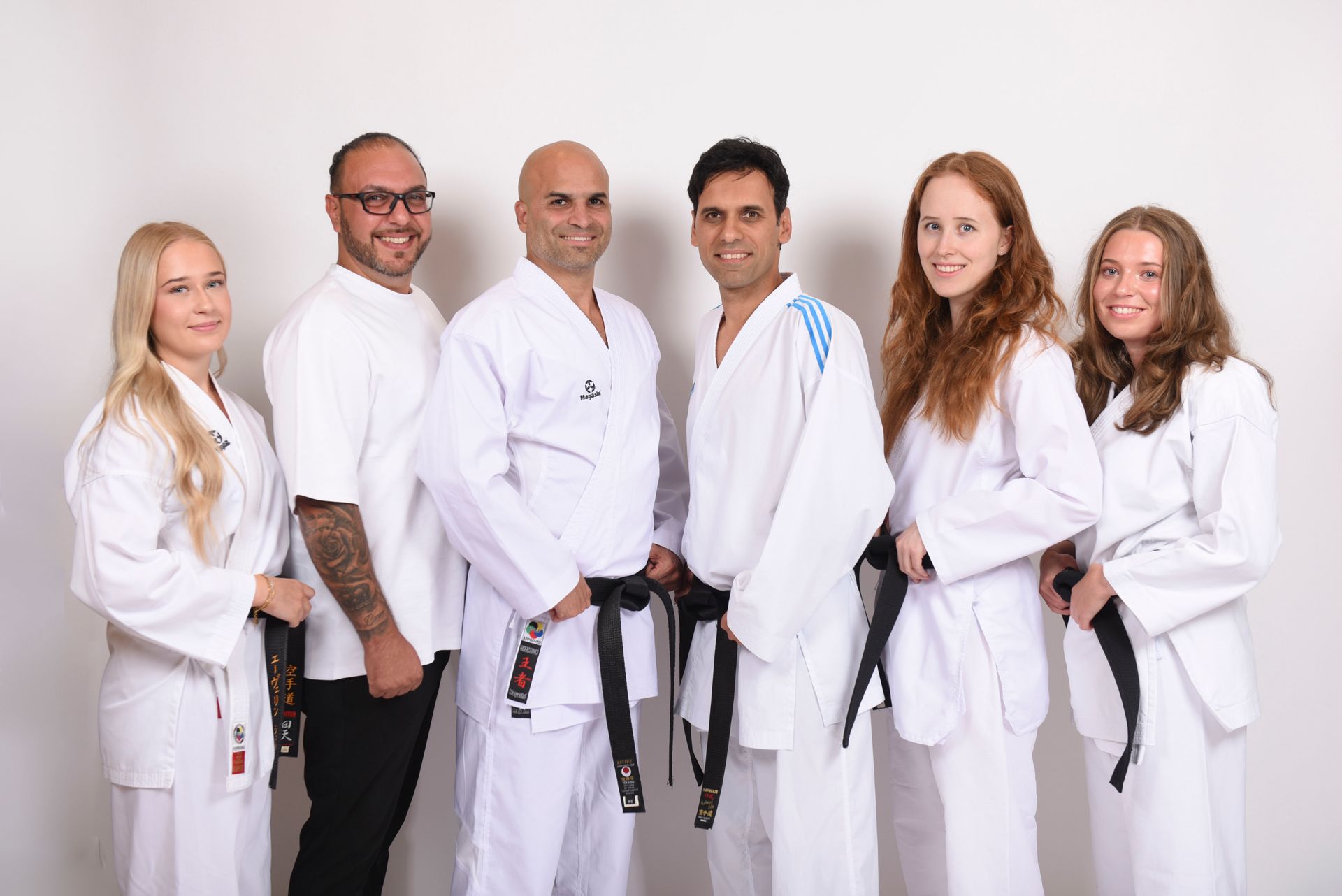 Gruppe von sechs Personen in Karateuniformen mit schwarzen Gürteln, die vor einem weißen Hintergrund für ein Foto posieren.