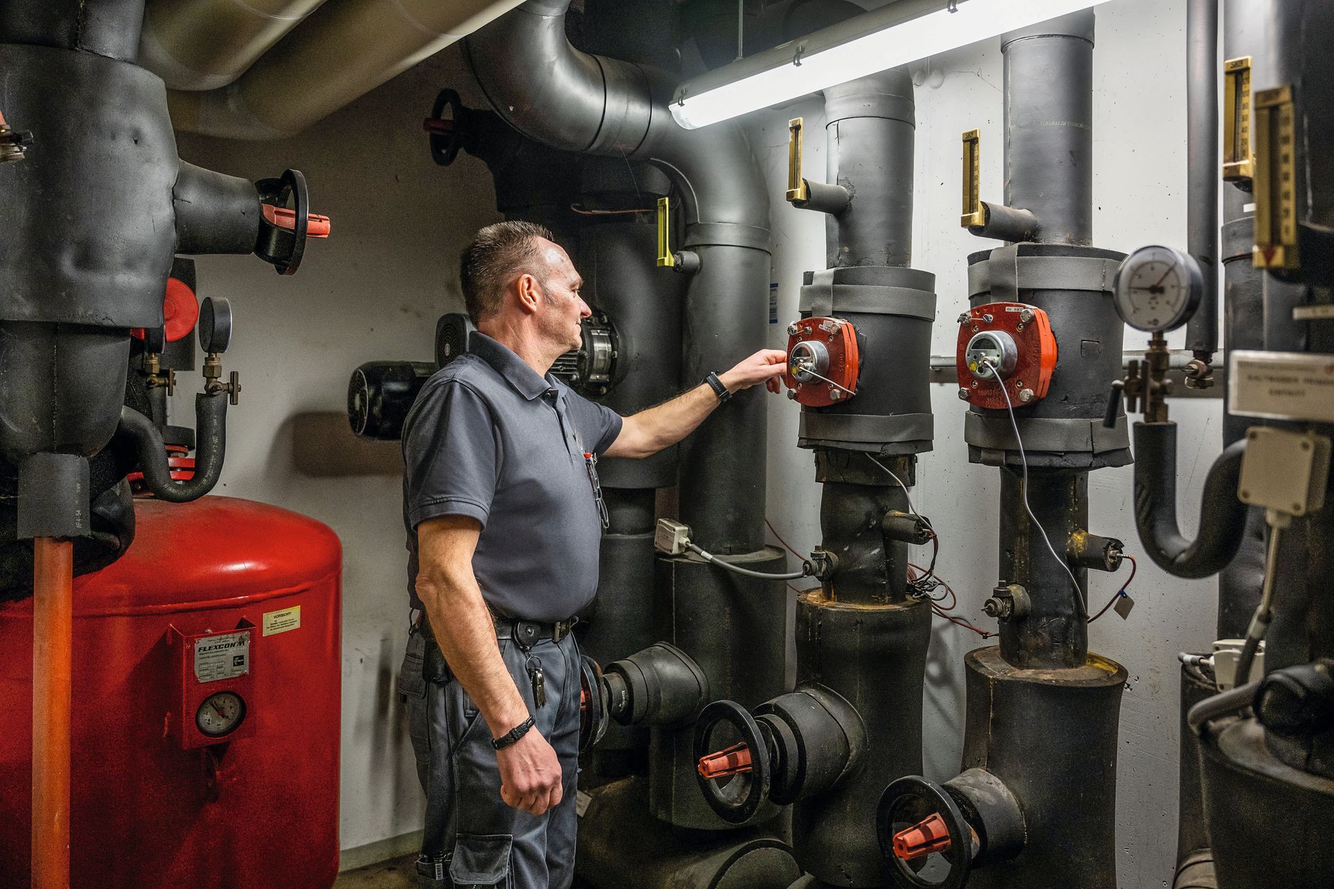 A man is standing in a room with a lot of pipes and valves.