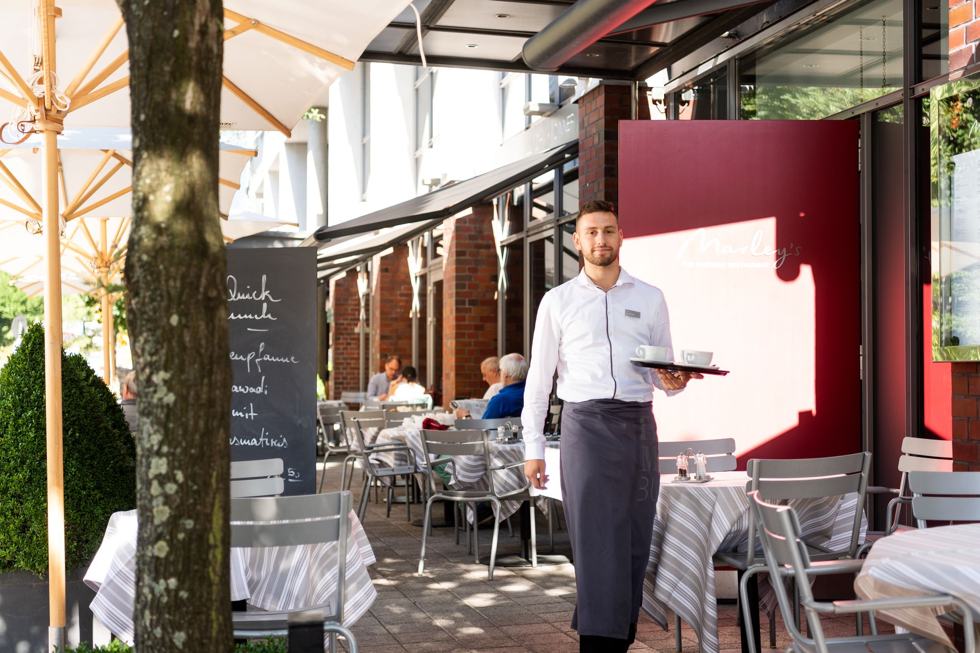 A waiter is holding a tray in front of a restaurant.