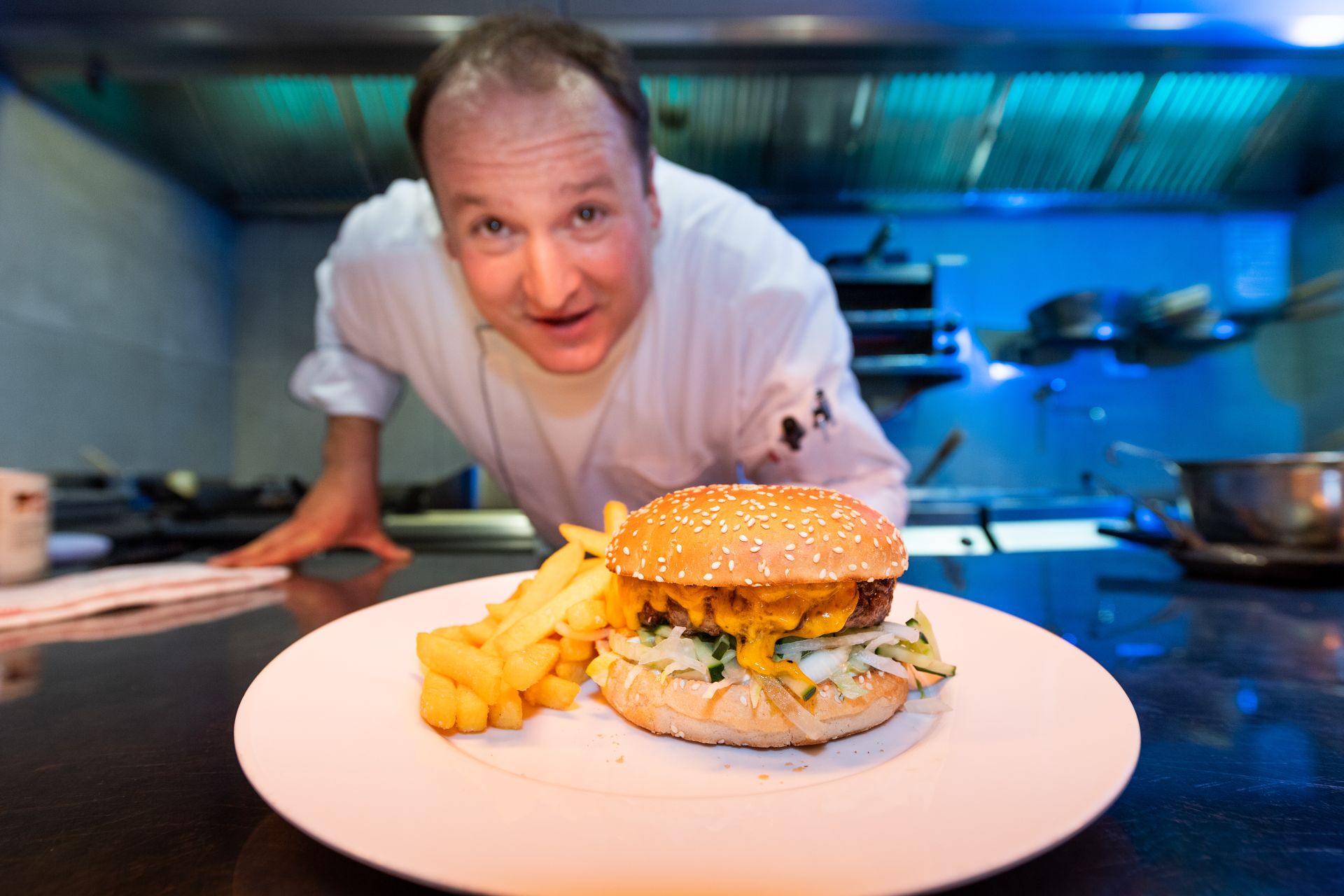 A chef is standing in front of a plate of food with a hamburger and french fries on it.