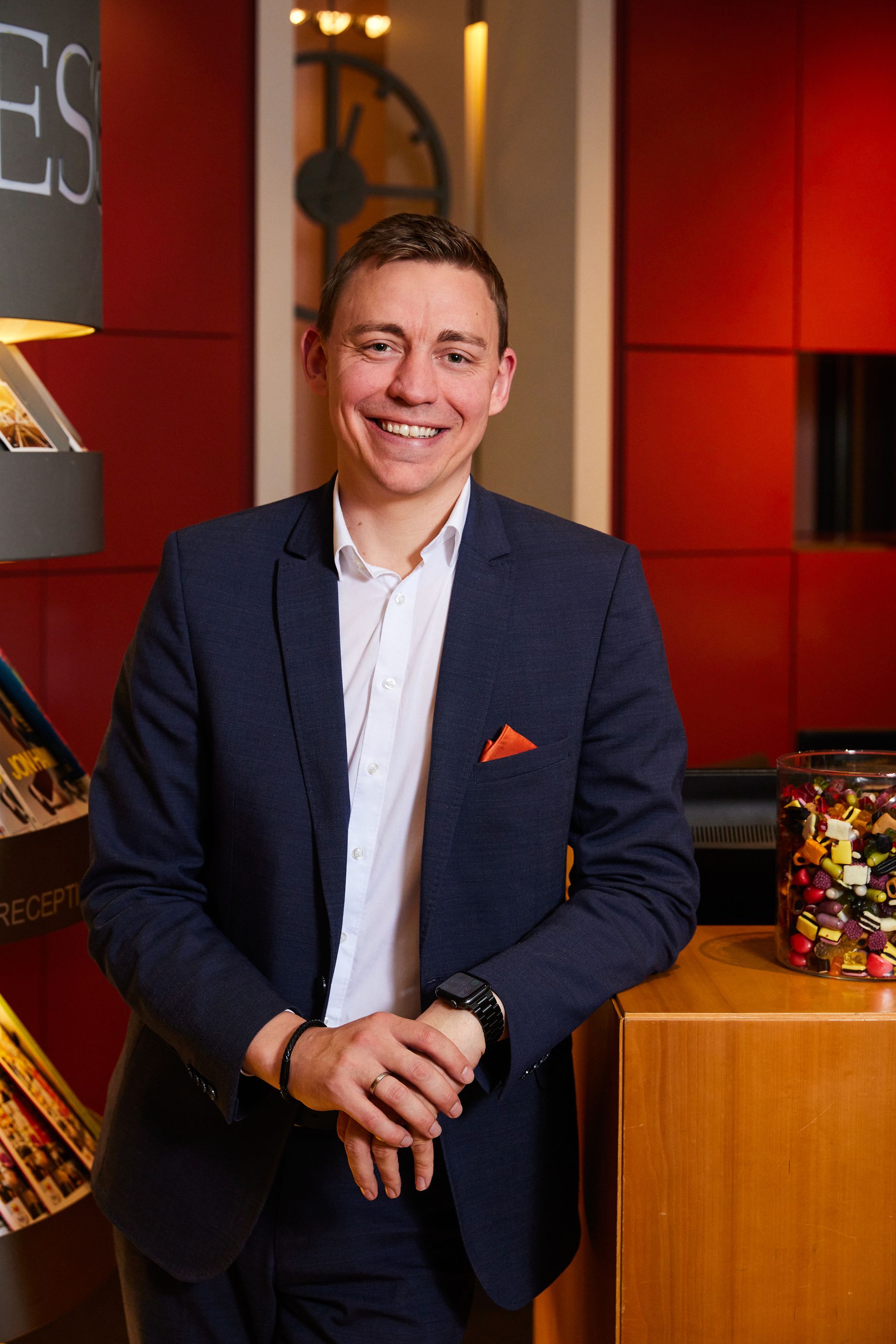 A man in a suit and white shirt is standing in front of a jar of candy.