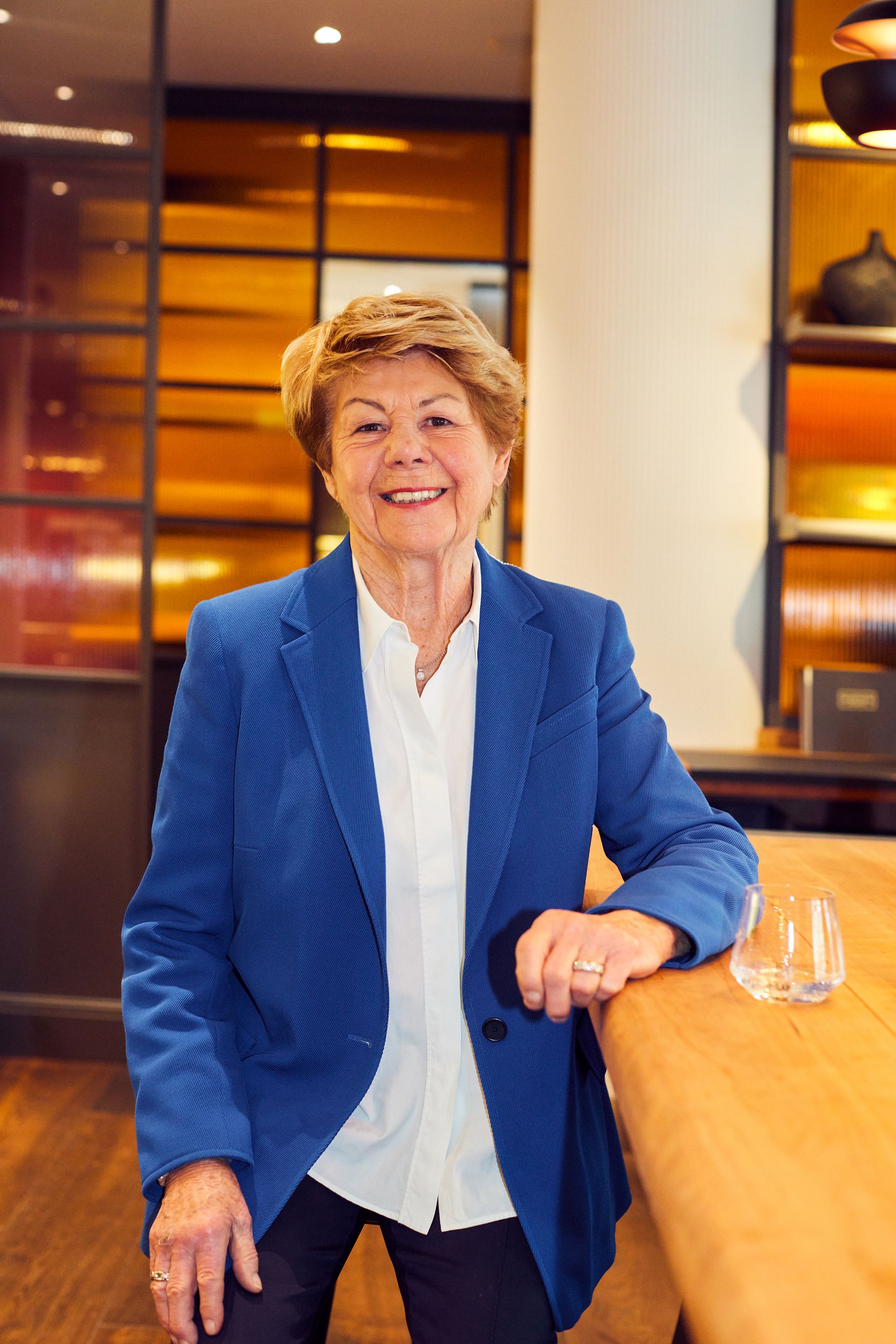 A woman in a blue jacket is leaning on a wooden table.