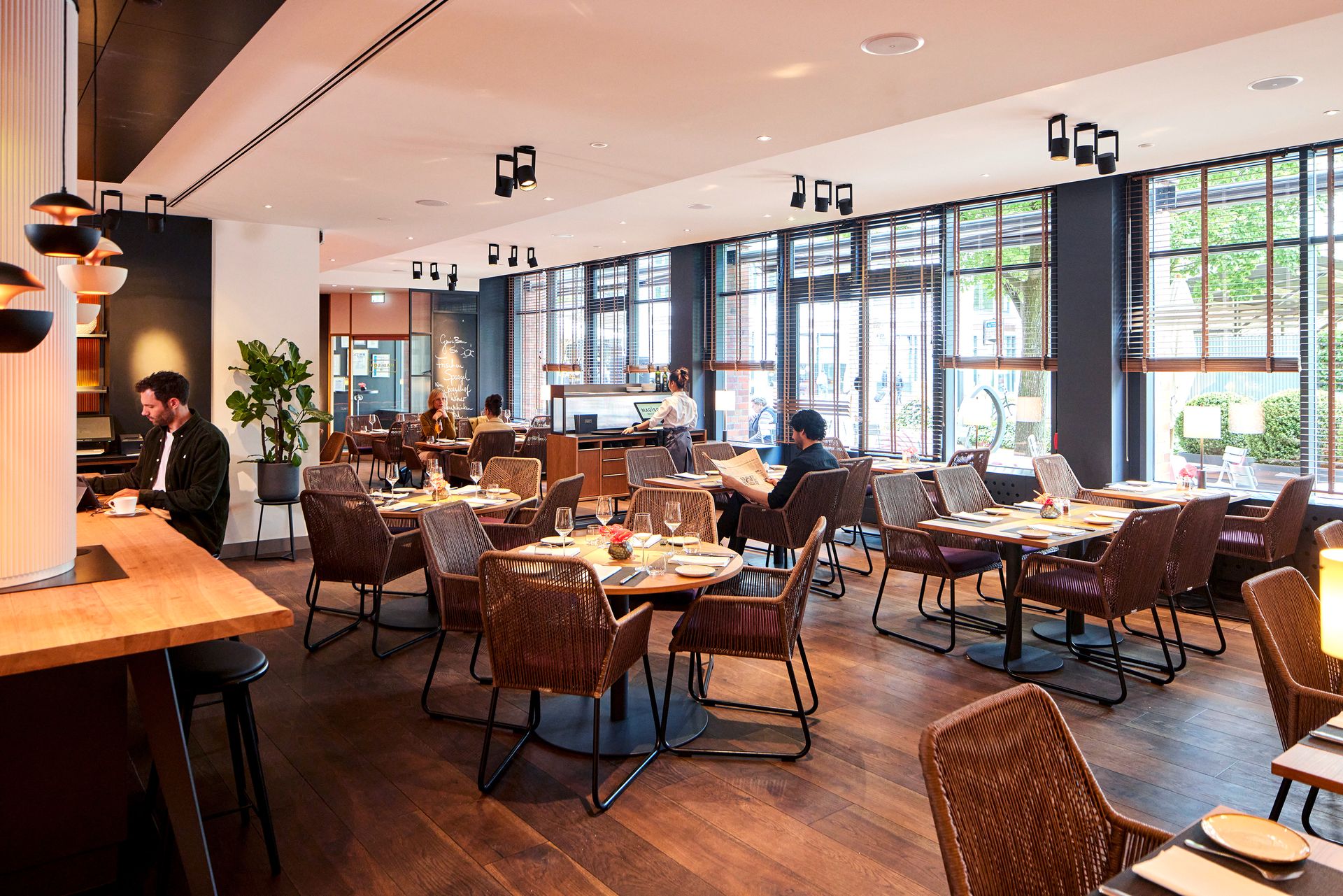 A restaurant filled with tables and chairs and a man standing at a counter.