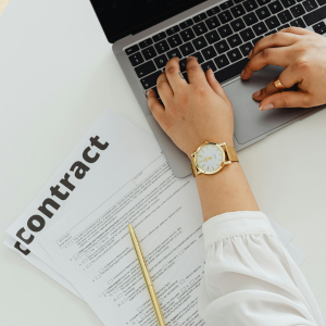 Una mujer está escribiendo en una computadora portátil junto a un contrato.