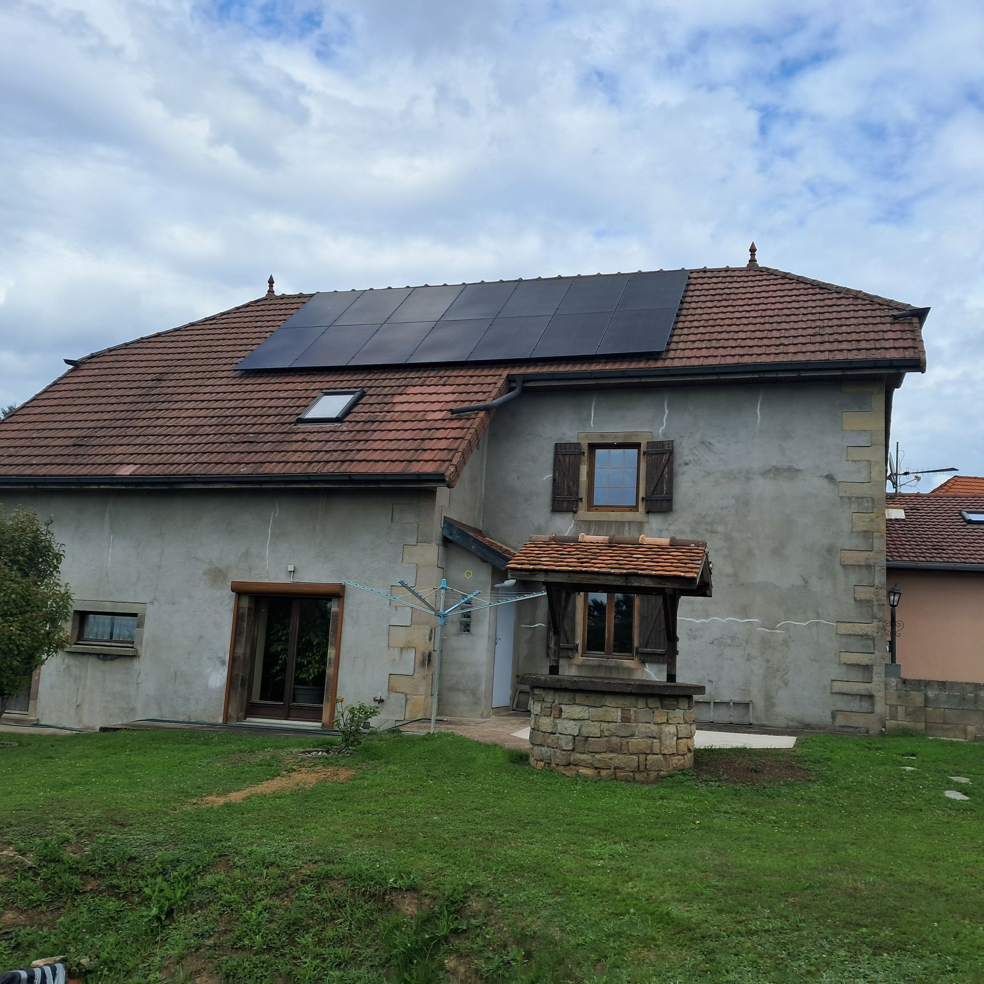 Maison au toit de tuiles sombres et panneaux photovoltaïques.