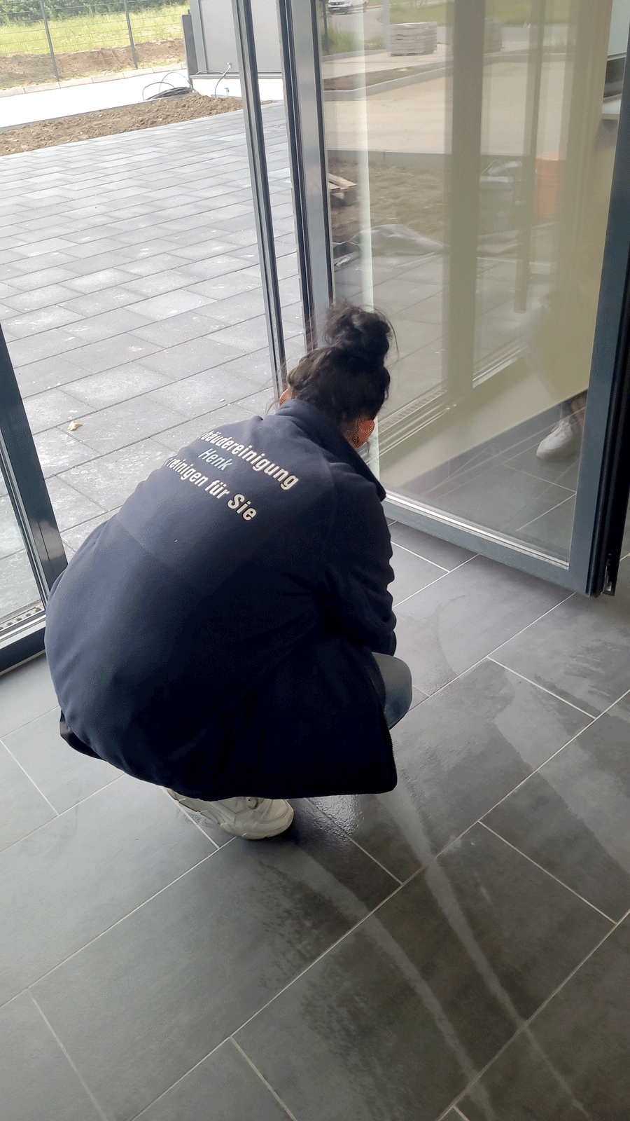 Eine Frau hockt vor einer Glastür und putzt den Boden.
